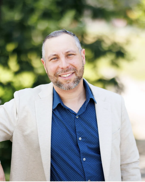 a man in a blue shirt and tan blazer wearing a rainbow kippah