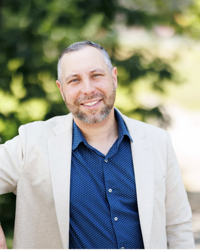 a man in a blue shirt and tan blazer wearing a rainbow kippah